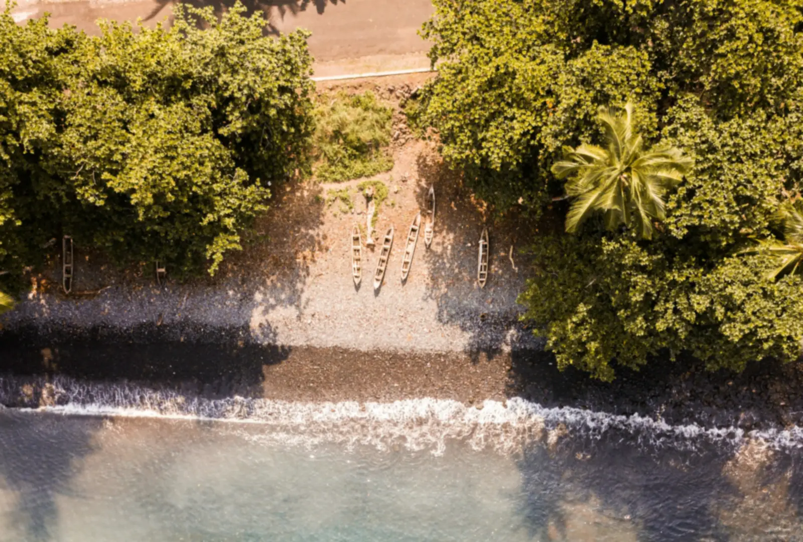 A black sand beach on São Tomé seen from above, with palms, dense green trees and clear turquoise water